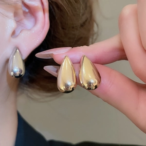 Close-up of sleek metallic water drop earrings in gold and silver finishes on a model