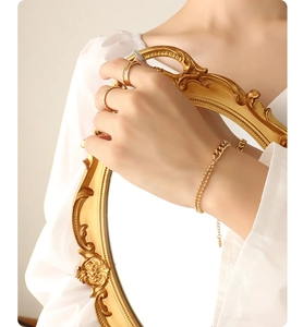 Detail of layered gold beaded bracelet and minimalist rings on model with vintage mirror