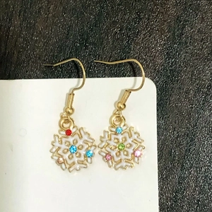 Detail of snowflake drop earring with colorful gemstones and white enamel in gold frame