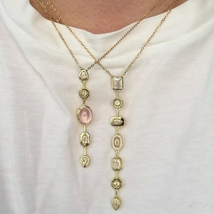 Close-up of layered gold necklaces with pink oval gemstone and square diamond pendants