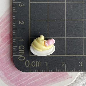 Macro view of small yellow resin duck charm with pink details on a scale mat for DIY crafts