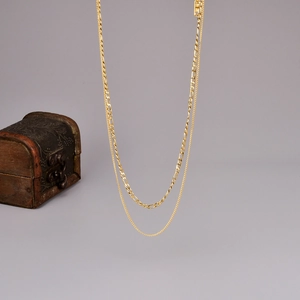 Detailed view of golden double-layer necklace with Figaro and O-chain links on wood box