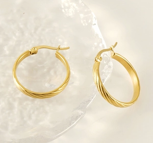 Close-up of golden vintage twisted hoop earrings on textured glass with soft lighting
