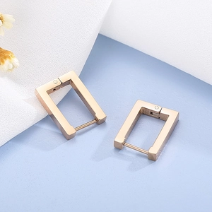 Detailed view of minimalist gold rectangular hoop earrings on soft textured fabric