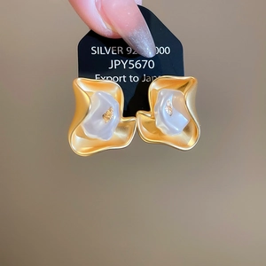 Detail of irregular matte gold wave earrings with white resin inlay and gold leaf
