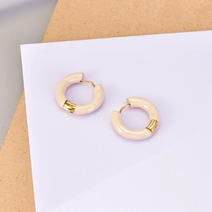 Gros plan de boucles d'oreilles créoles beiges et dorées sur carte de support