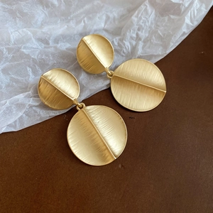 Detail of matte gold geometric drop earrings with brushed texture and metal finish