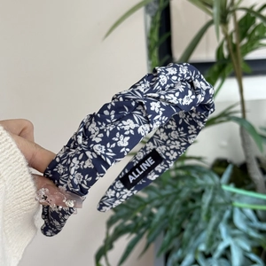 Detailed view of dark blue floral fabric headband with knot design and brand label
