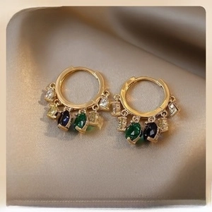 Detail of gold hoop earrings with multi-colored gemstone charms on satin fabric
