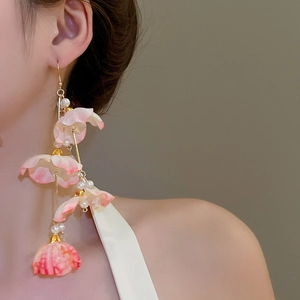 Détail de boucles d'oreilles à pompon floral avec pétales dégradés roses et perles