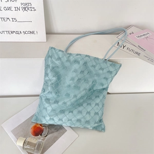 Detailed view of light blue quilted tote bag with thin straps on a minimalist shelf