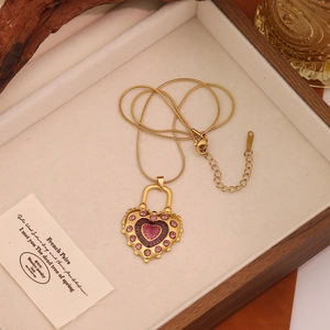 Detail of gold snake chain necklace with pink zircon heart pendant on wooden tray