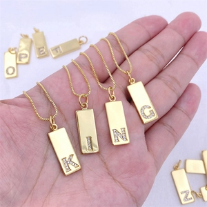 Gold rectangular alphabet pendant necklace with zircon crystals held in hand
