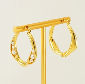 Detail of irregular gold twist hoop earrings with embedded white pearls on a display