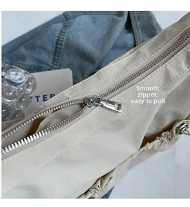 Detail of smooth silver metal zipper and wrinkled nylon fabric on beige shoulder bag