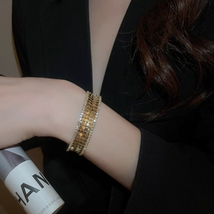 Detail of gold wide bangle with honeycomb texture and crystals on black suit sleeve