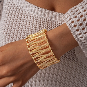 Detail of a gold wide-band wire-wrapped open bangle featuring geometric woven metal textures