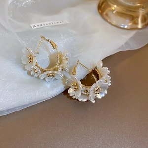 Detail of flower earrings with gold hoop, white shell petals and small rhinestones
