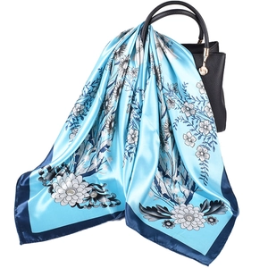 Blue floral satin silk scarf with flower patterns draped on a black leather handbag