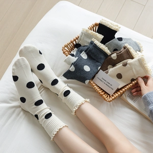 Calze con bordo in pizzo e pois in beige e grigio esposte su pavimento in legno