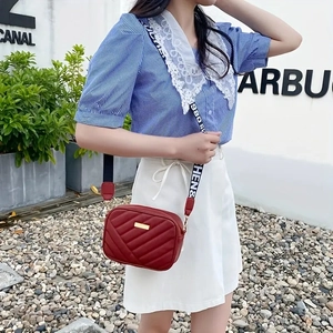 Detail of red quilted crossbody bag with gold logo plate and wide lettered strap