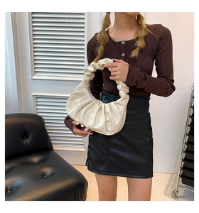 Detailed view of cream ruched cloud handbag styled as an underarm bag on a model