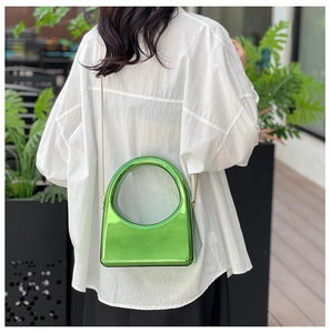 Detail of bright green acrylic evening bag with gold chain and circular cutout handle