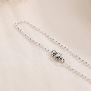 Detail view of a white beaded chain with silver metal links and a lobster clasp