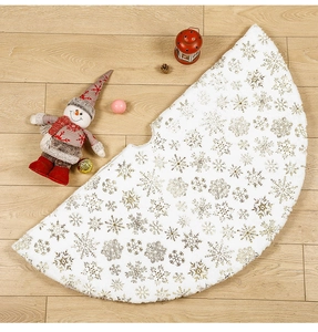 Detail of white plush Christmas tree skirt featuring golden snowflake patterns on wood floor