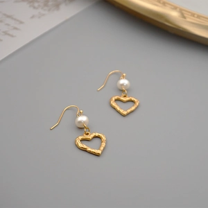 Elegant gold hollow heart earrings with white freshwater pearls on a grey background