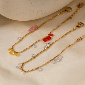 Three gold beaded bracelets with colorful zircon water drop pendants on beige silk