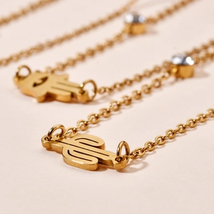 Macro shot of gold necklace pendants featuring cactus and Hamsa hand motifs with zircon