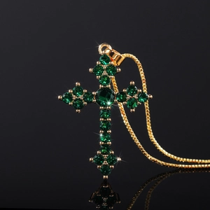Macro shot of gold cross pendant necklace featuring inlaid green zircon on black background