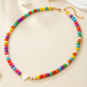 Detailed shot of multi-color beaded necklace with a white heart charm on a textured background