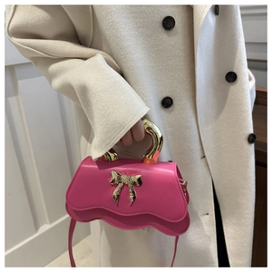 Detail of rose pink leather handbag with gold metal bow and polished curved handle