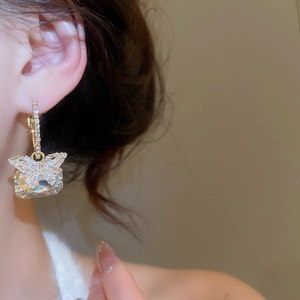 Macro shot of gold butterfly drop earring with square zircon stones on model's ear