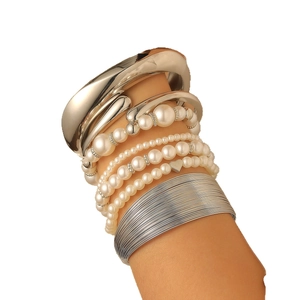 Stacked layered bracelet set featuring gold bangles, white pearls, and a heart charm