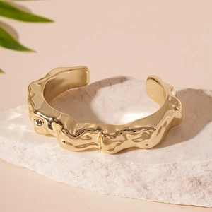 Detailed close-up of a gold cuff bracelet featuring irregular molten lava texture on a stone