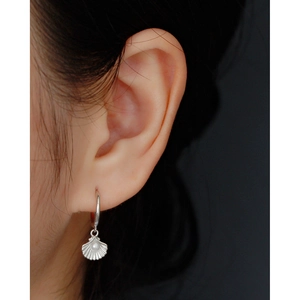 Macro shot of silver shell hoop earring with white pearl detail on model's ear