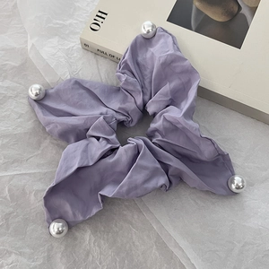 Detail of purple fabric scrunchie with corner pearls on a minimalist background