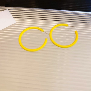 Detailed view of matte yellow C-shaped hoop earrings on a textured minimalist surface