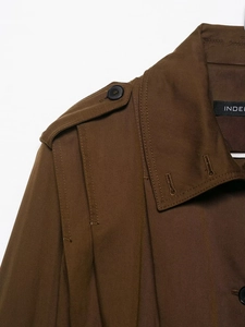 Detail view of brown trench coat shoulder tab with black button and twill texture