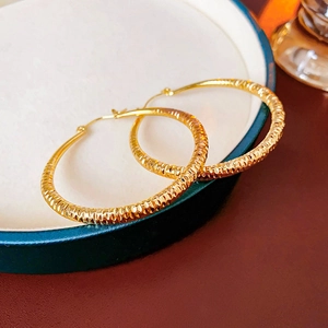 Gros plan de boucles d'oreilles anneaux texturées dorées sur un plateau en céramique