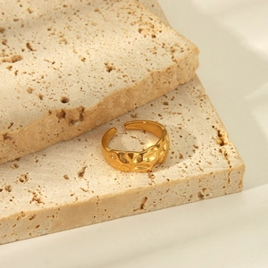 Detailed view of hammered gold stainless steel open ring on natural beige stones