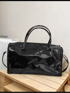 Large black patent leather travel bag with handles on wooden tray for fitness or travel