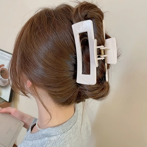 Close-up of a large beige square hair claw clip securing a low bun on dark hair