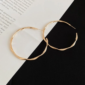 Detailed view of gold twisted metal hoop earrings with elegant wavy texture on paper