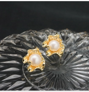 Macro shot of gold-plated irregular pearl stud earrings on textured glass with black background
