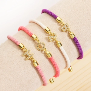 Close-up of woven rope bracelets with sparkling rhinestone letter charms on a jewelry stand