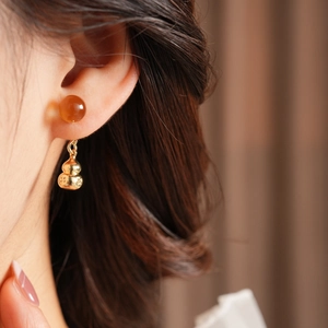 Close-up of model wearing a retro golden gourd pendant earring with amber beads